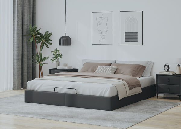 Dark grey upholstered ottoman bed with beige bedding and dark bedside tables in a styled bedroom.