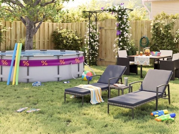 Sunny backyard garden with an above-ground swimming pool, pool noodles, goggles, beach ball, and flip-flops on the grass. Two black metal sun loungers with grey cushions sit beside a small side table, while an outdoor dining set with dark rattan chairs is arranged near a flowering pergola, wooden fence, garden plants, and summer party accessories.
