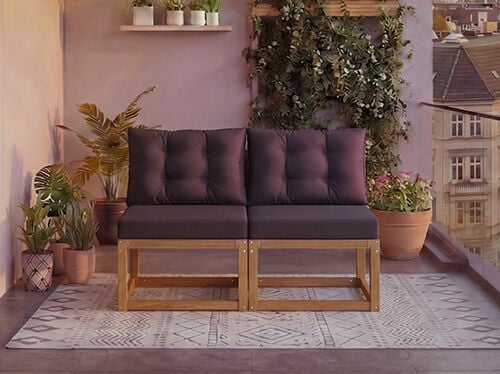 Two-seat modular wooden sofa with dark grey cushions on a balcony surrounded by potted plants and a city view in the background