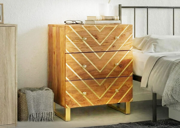 Wooden bedside table with three drawers, featuring a geometric gold pattern, placed next to a bed in a bright bedroom interior.