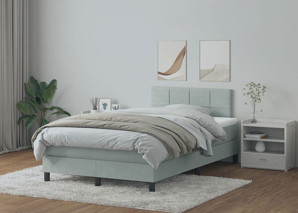 Light grey boxspring bed with panelled headboard, white bedding, and light wood bedside table and vanity table in a styled bedroom.