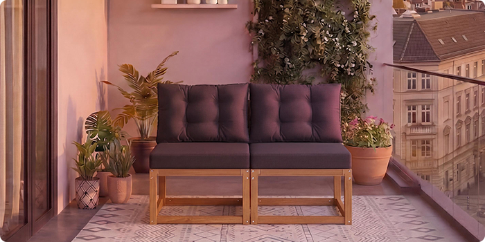 Two-seat modular wooden sofa with dark grey cushions on a balcony surrounded by potted plants and a city view in the background