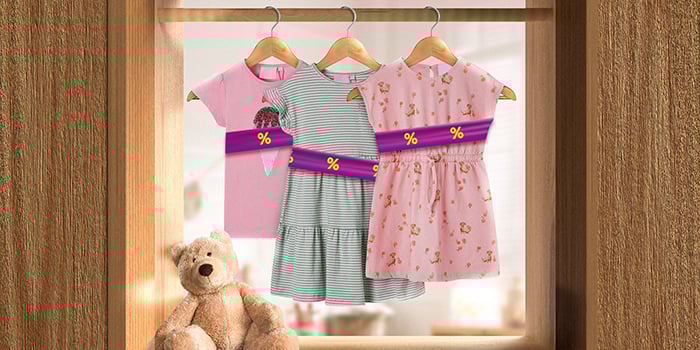 Kids' clothes on hangers wrapped in a purple promotional band with yellow discount icons, hanging on a rail indoors. Click to see the products in the offer.